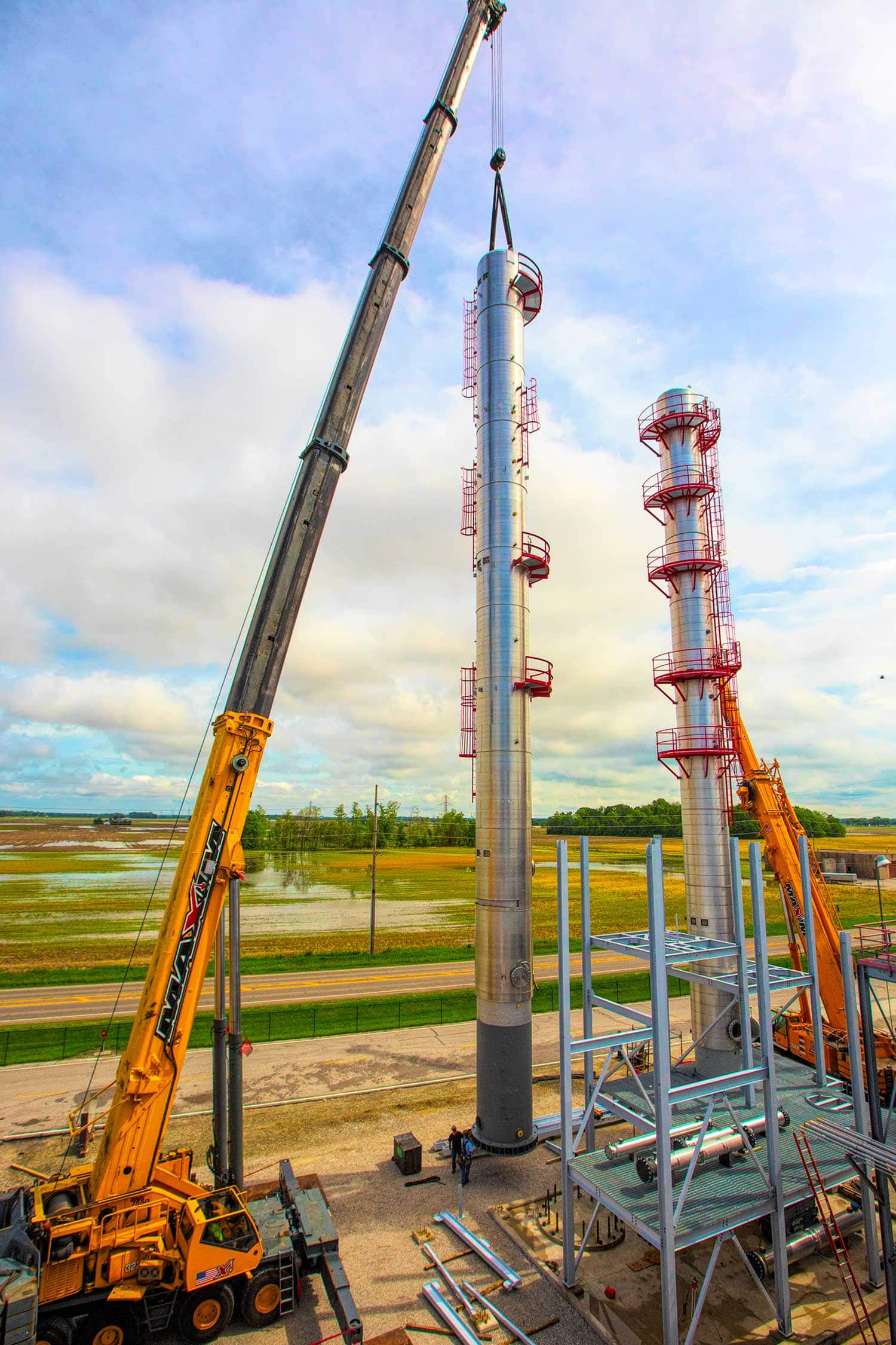 Crane lifting a distillation column into place at an industrial processing facility construction site.