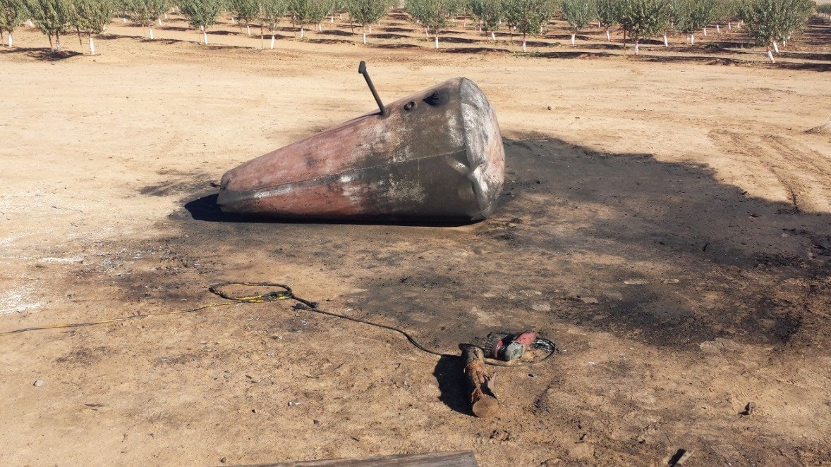 Damaged tank from explosion: Tank ends are bowed outward. No emergency venting evident. Small grinder with wire brush wheel near-by.
