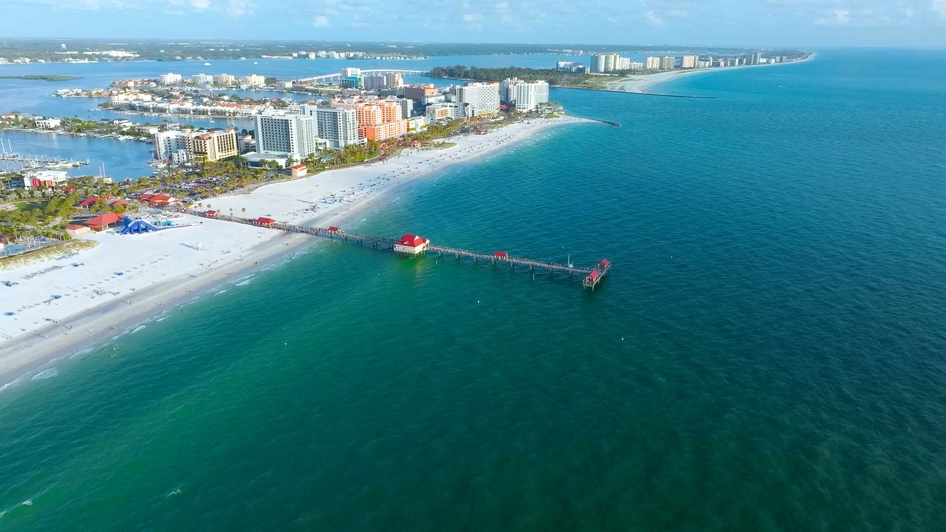 Aerial view of Clearwater Beach, Florida, with white sand, turquoise water, and a long pier extending into the Gulf of Mexico.