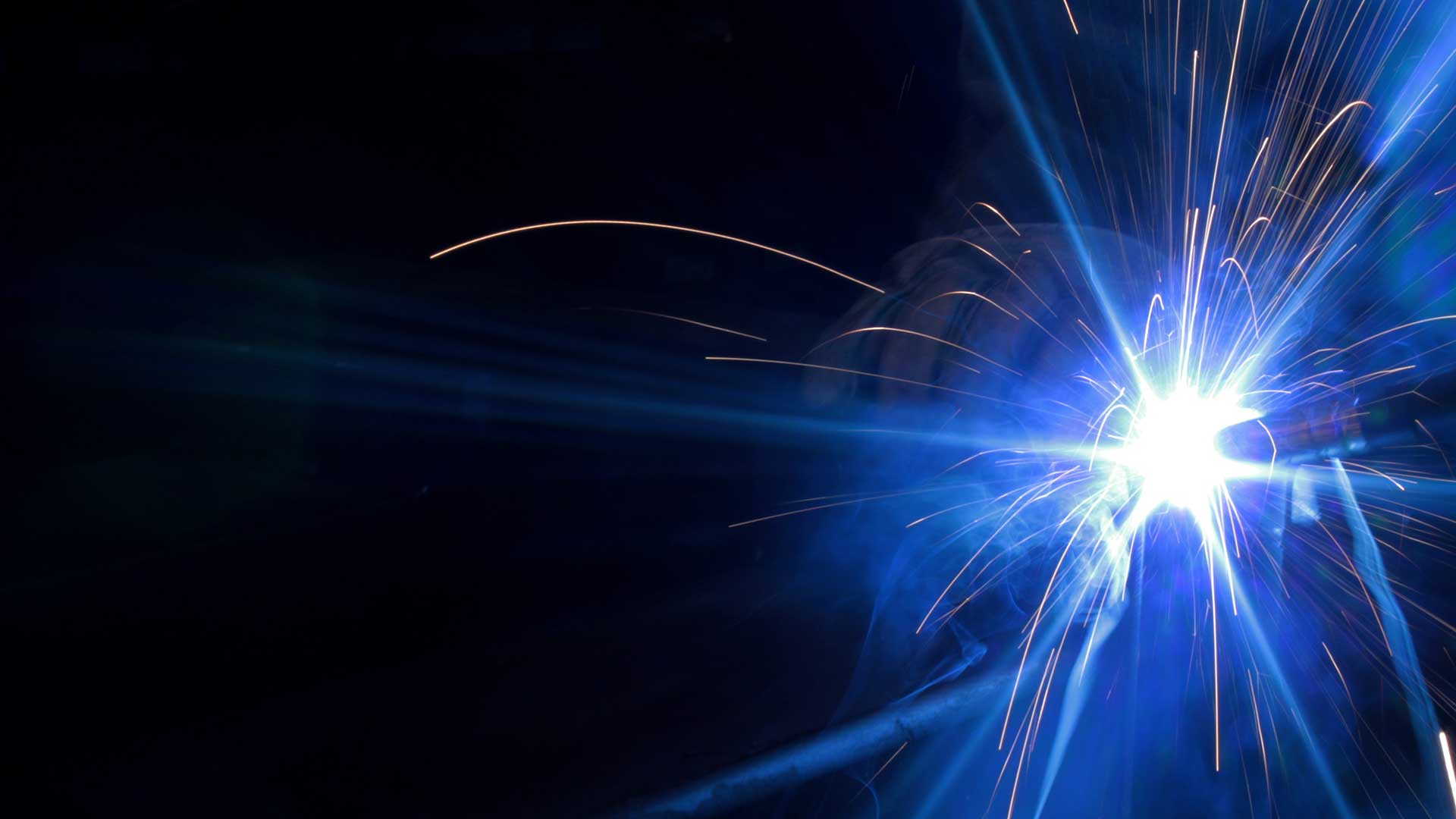 Bright welding arc with sparks illuminating a steel weld in progress.