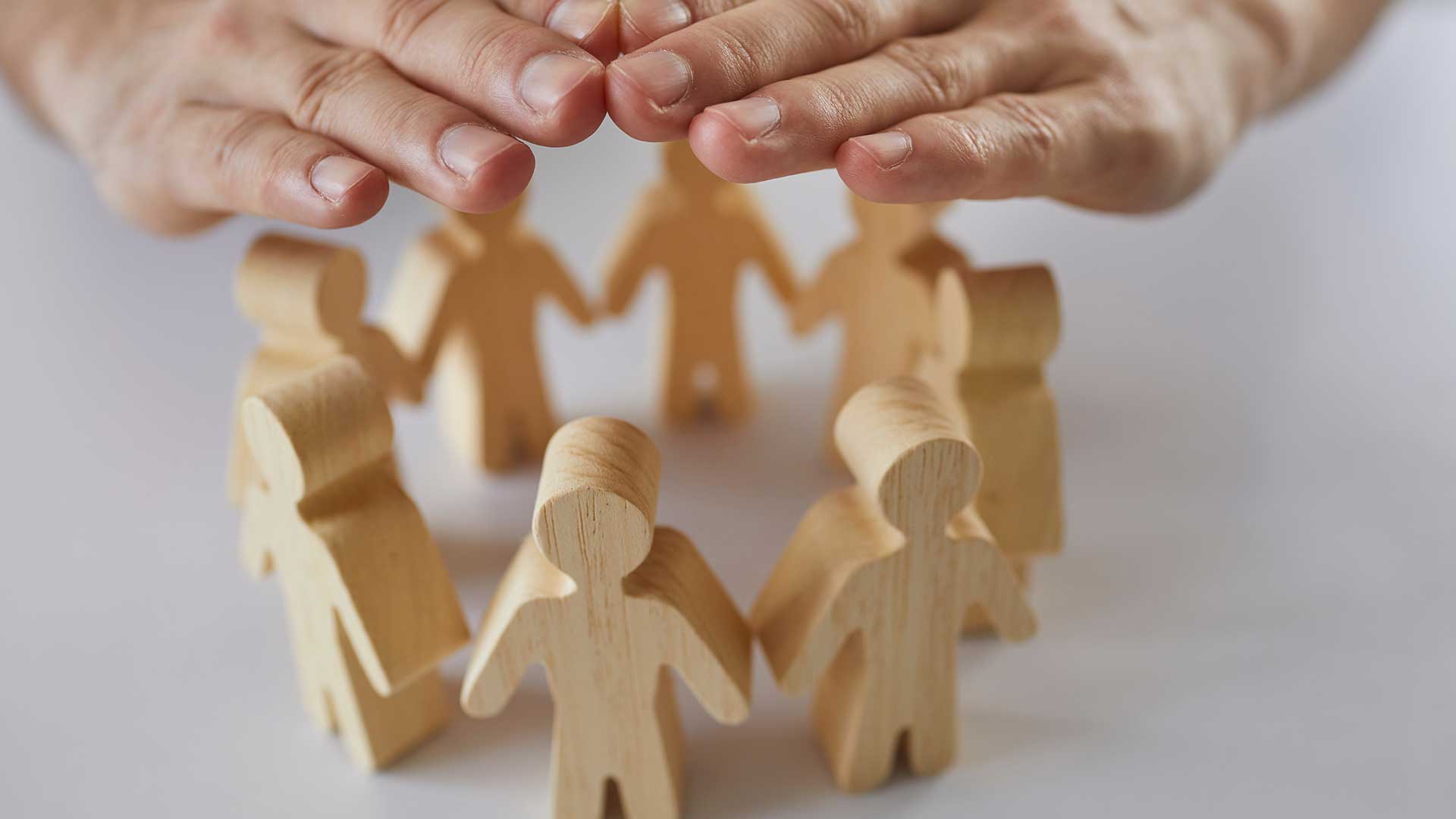 Hands shielding a circle of wooden human figures, symbolizing protection and community safety.
