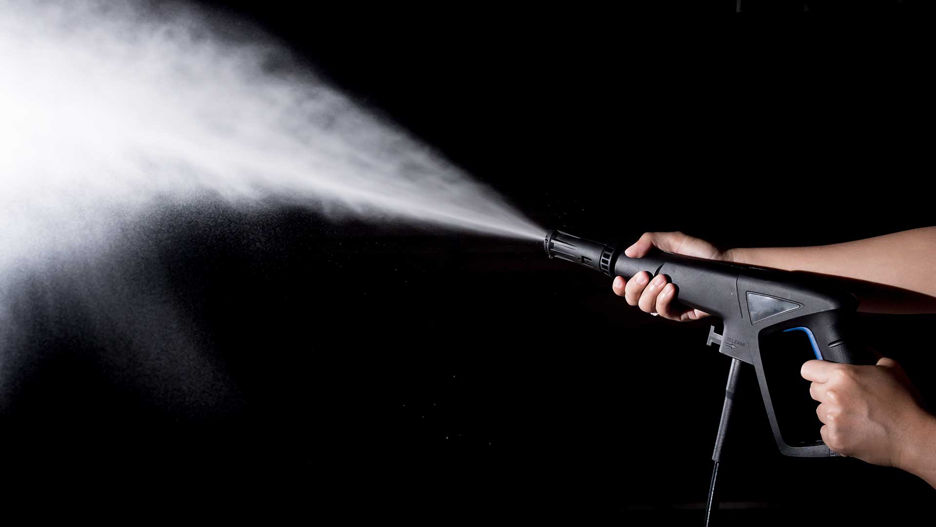 Person using a pressure washer spraying a powerful stream of water against a dark background.