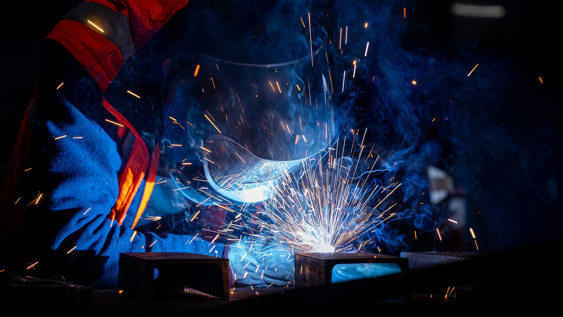 Welder wearing protective gear working during metal fabrication in a fabrication shop.