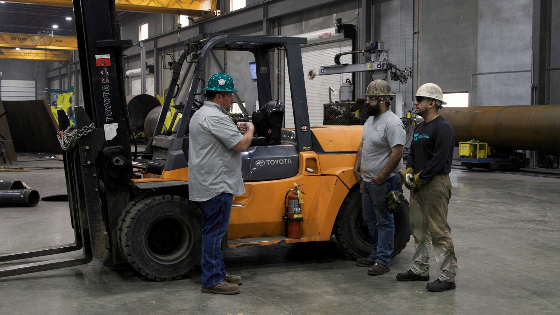 Three workers in hard hats discussing forklift safety near a forklift.