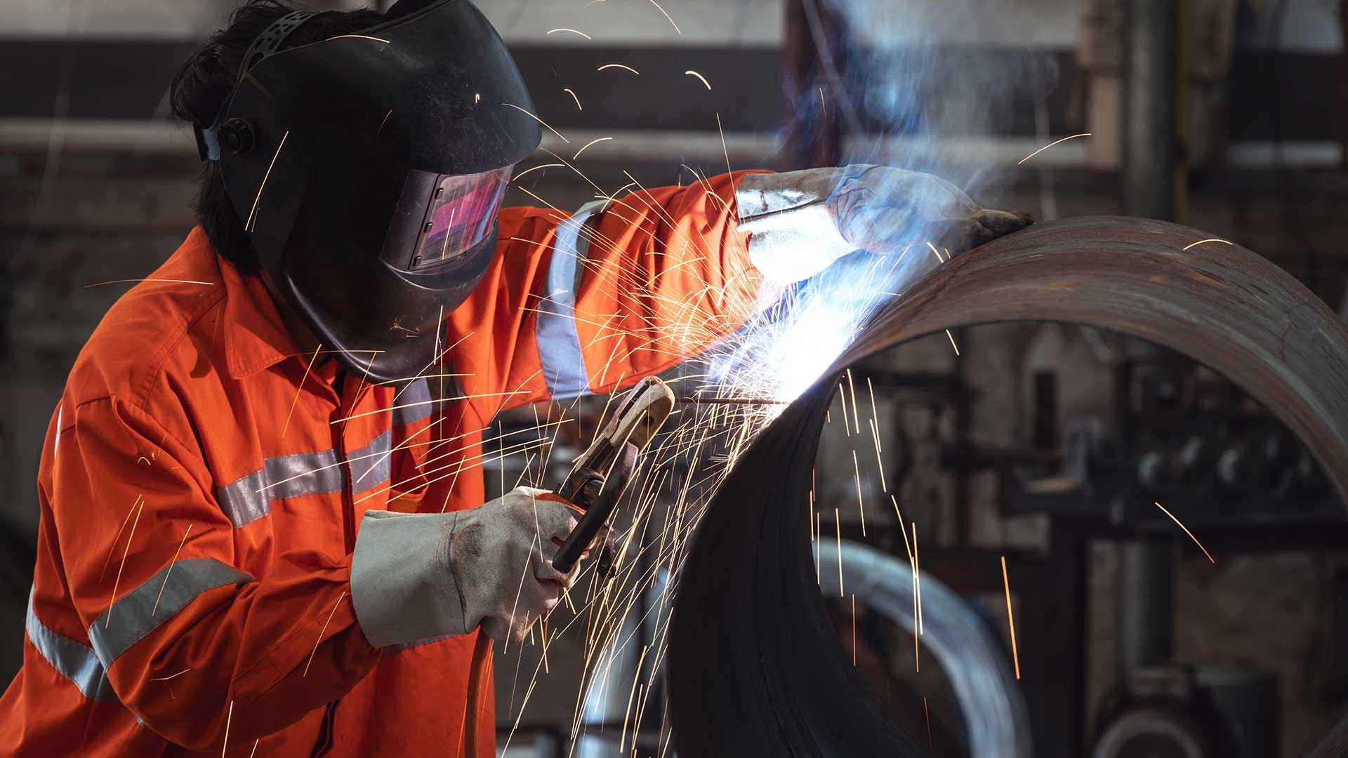 Welder with a protective face mask welding steel pipe