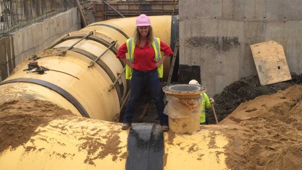 Woman in PPE standing on top of steel water pipe.