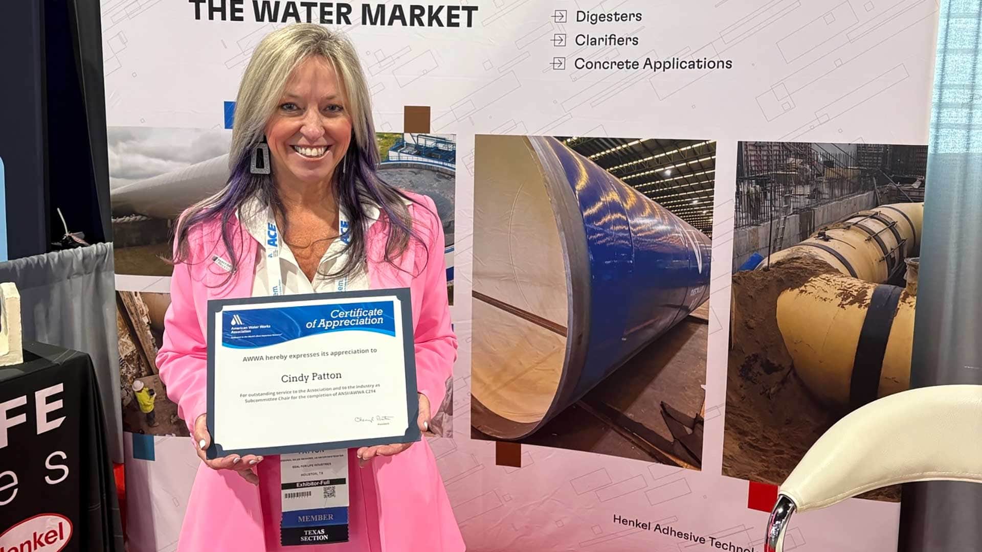 Woman holding certificate of appreciation standing in trade show booth.