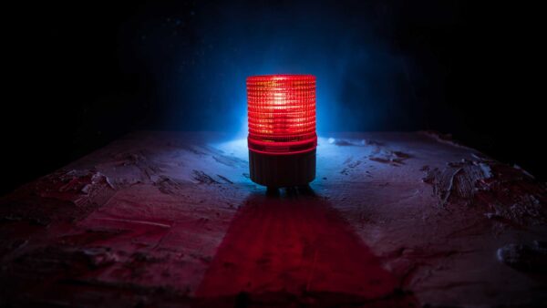Red emergency warning light glowing on a dark industrial surface with blue backlight.