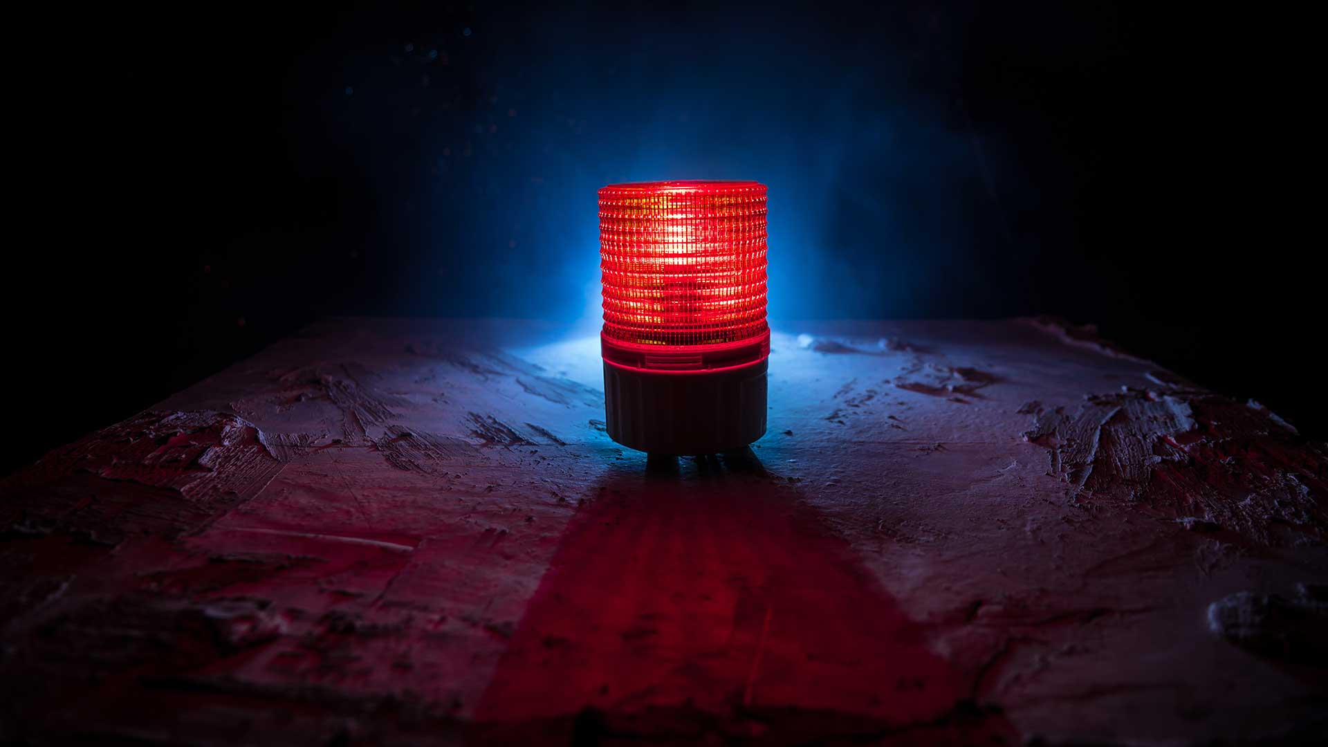 Red emergency warning light glowing on a dark industrial surface with blue backlight.