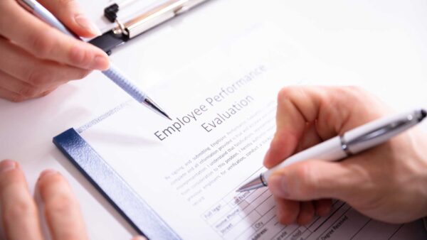 Two people reviewing and signing an employee performance evaluation form on a clipboard.
