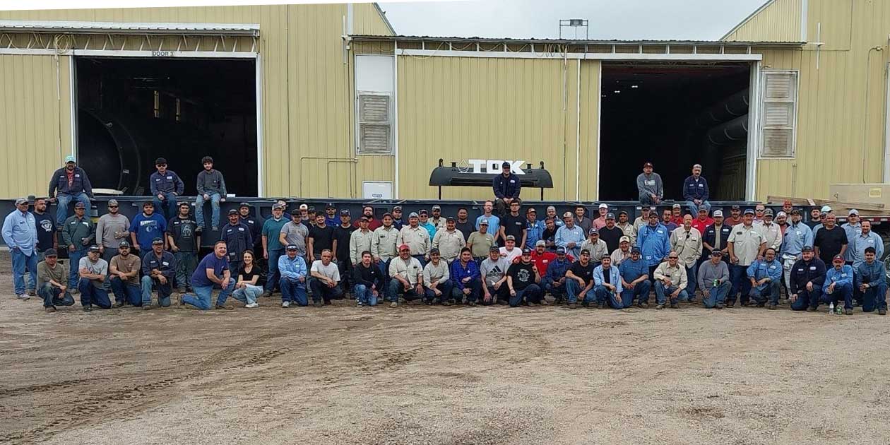 Group photo of employees standing together outside a manufacturing facility at Tex-Ok-Kan Oil Field Services.