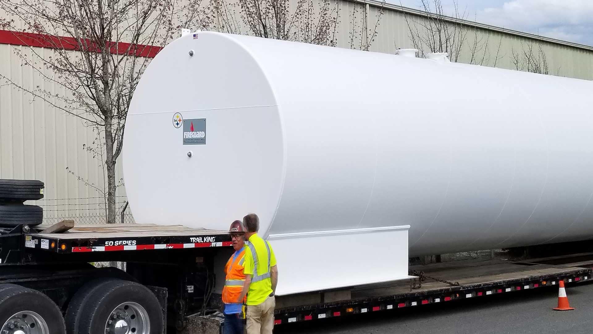 Truck shipping a FIREGUARD® double-wall steel storage tank outside an industrial facility with workers guiding the placement.
