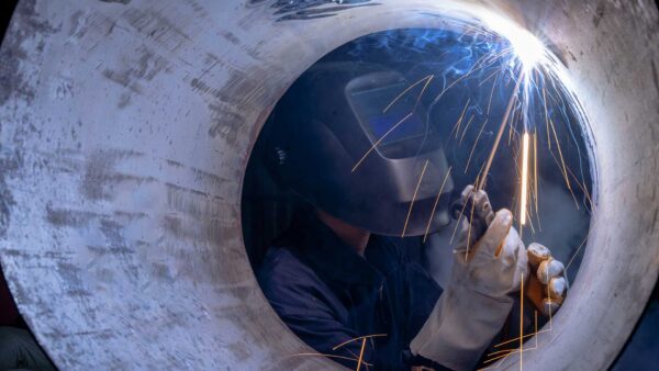 Welder performing interior welding inside a steel pipeline with sparks and protective gear.