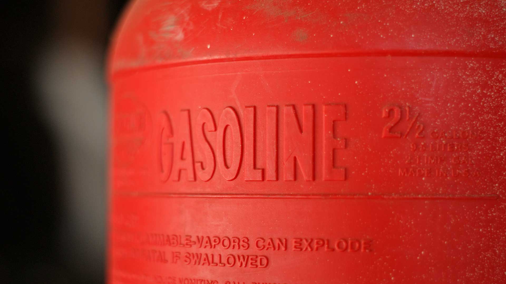 Close-up of a red gasoline container with embossed “Gasoline” label and flammable vapor safety warnings.