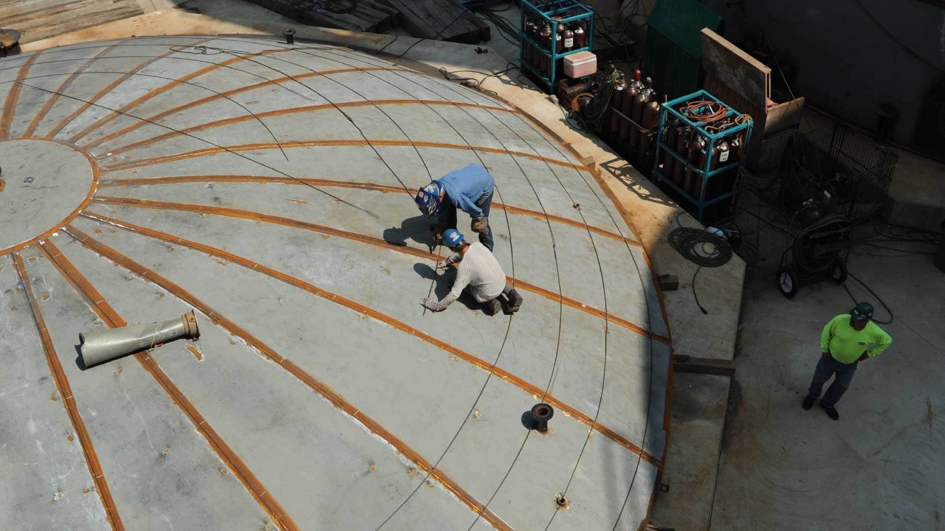 Workers installing radial roof rafters on an aboveground steel storage tank during construction.