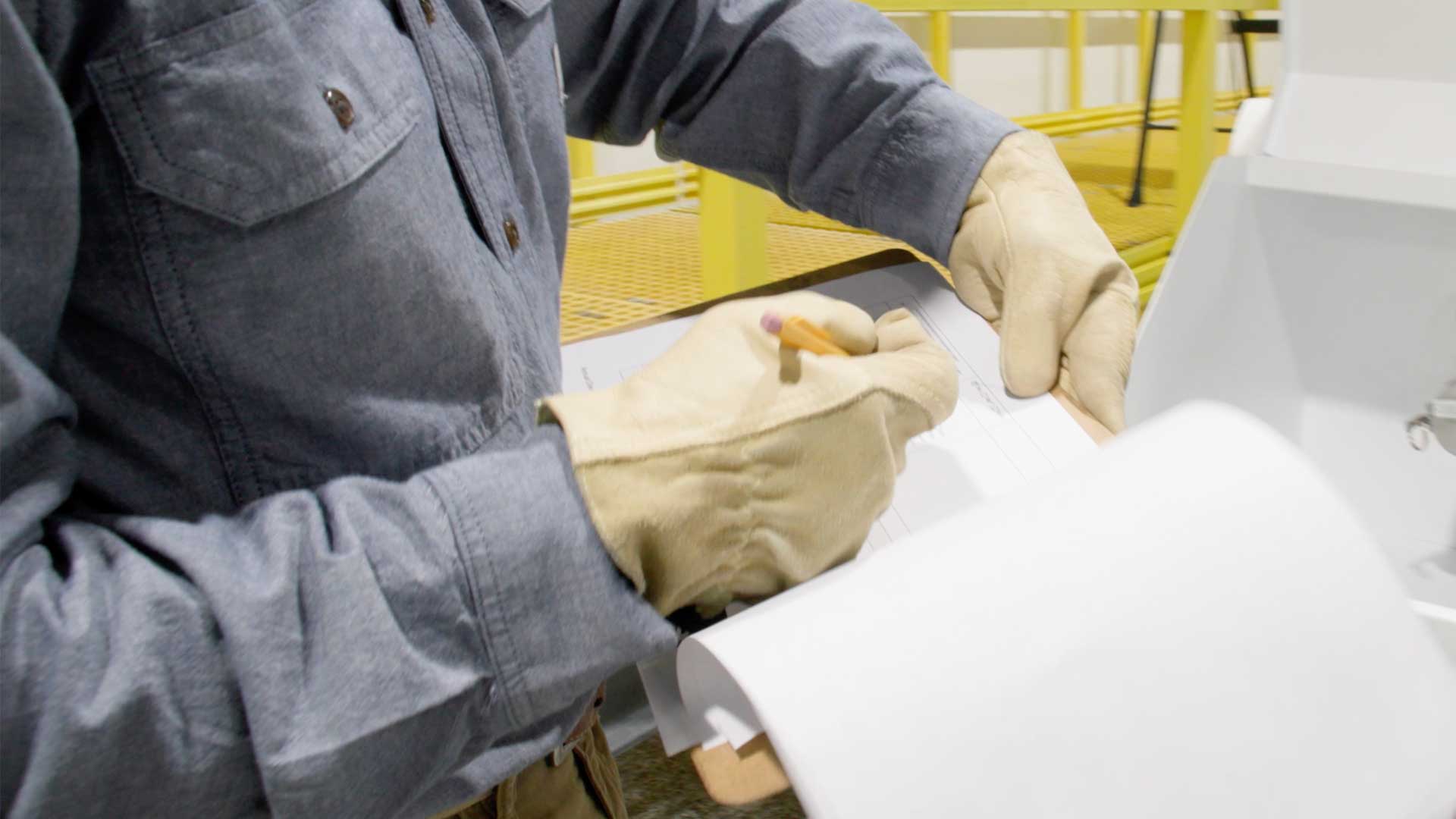 Worker wearing gloves and protective clothing completing an inspection checklist on-site.