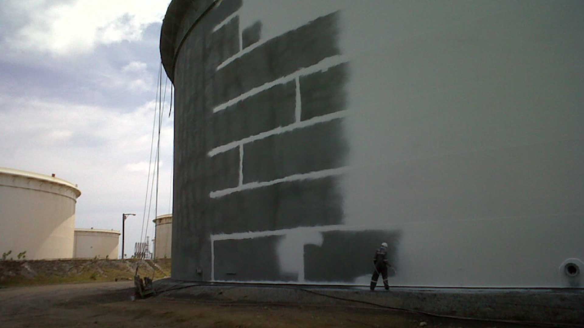 Worker applying protective coating to large aboveground steel storage tank for corrosion protection.