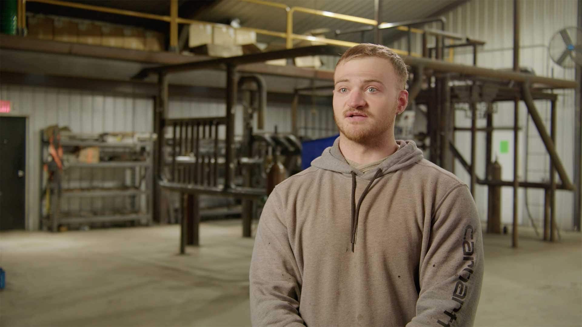 Young man speaking during an interview inside an industrial training facility.