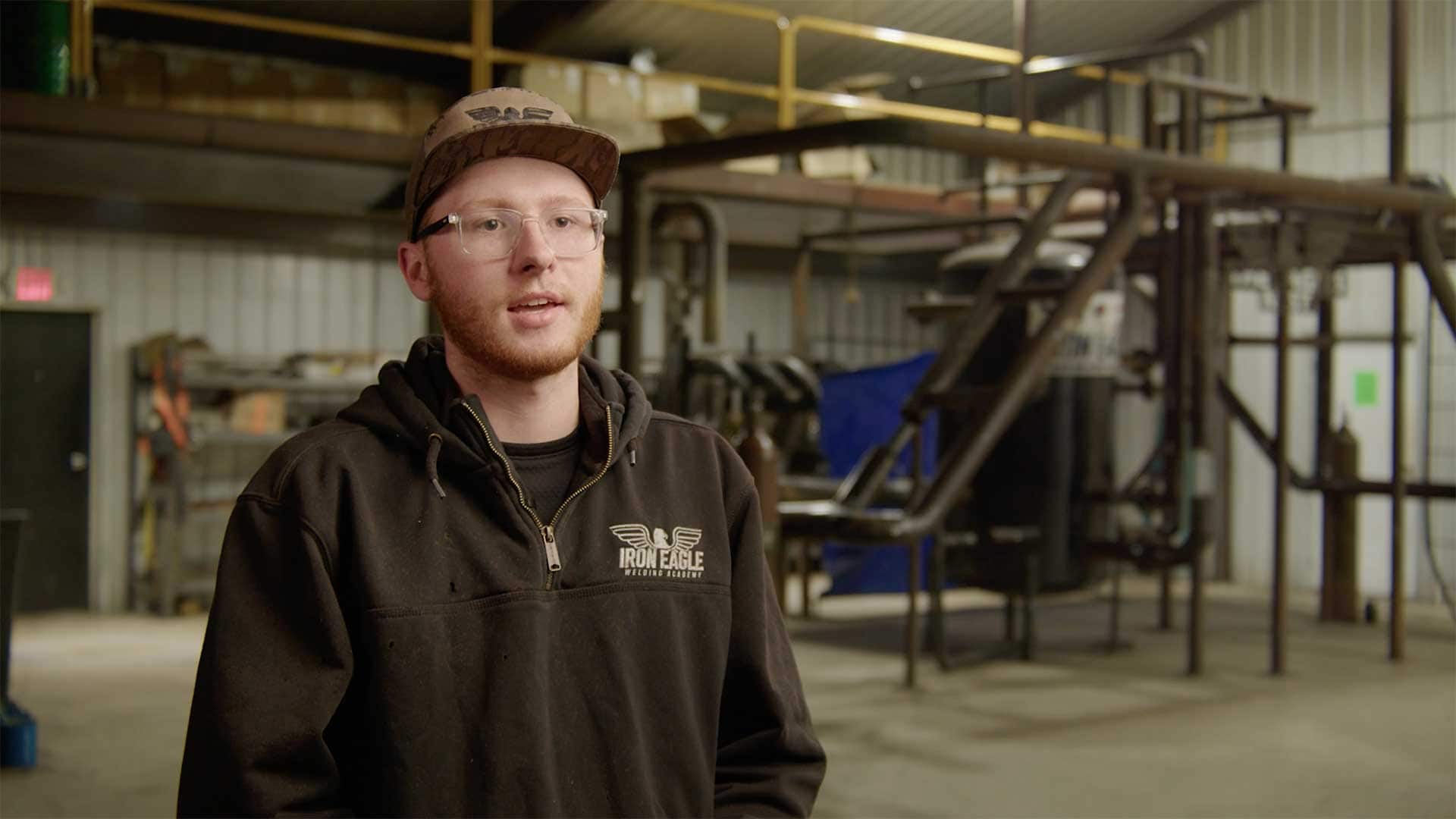 Young man speaking during an interview inside a welding and fabrication training facility.