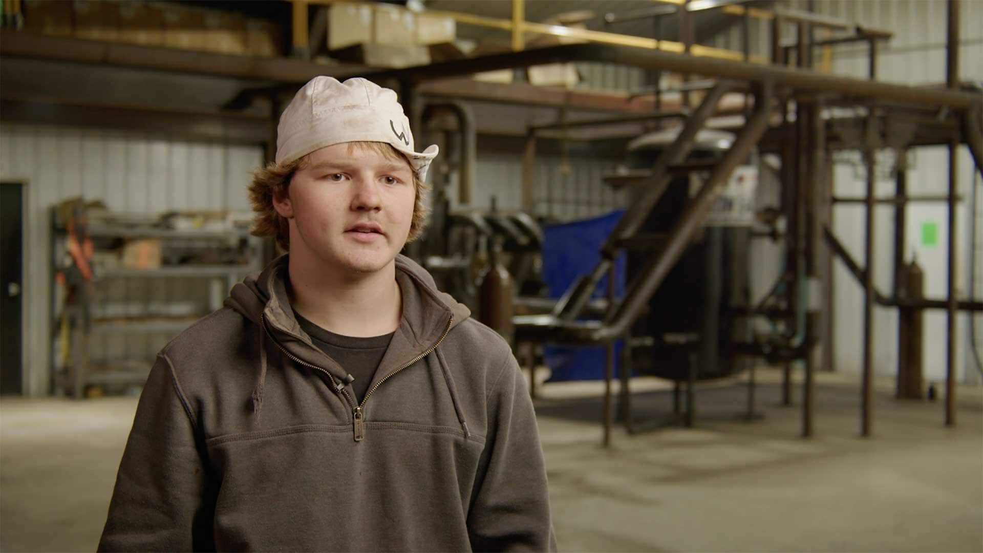 Young man speaking during an interview inside a welding and fabrication training facility.