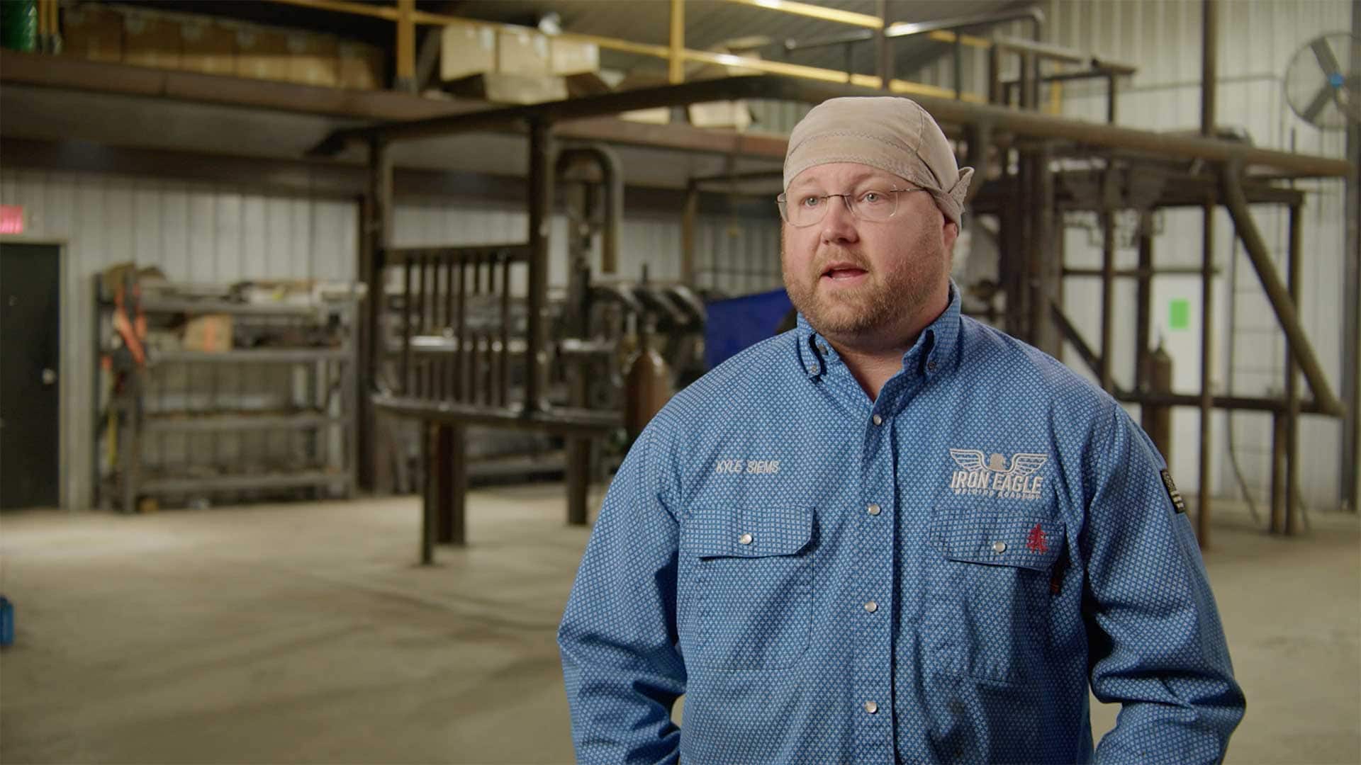 Man speaking during an interview inside a welding and fabrication training facility.