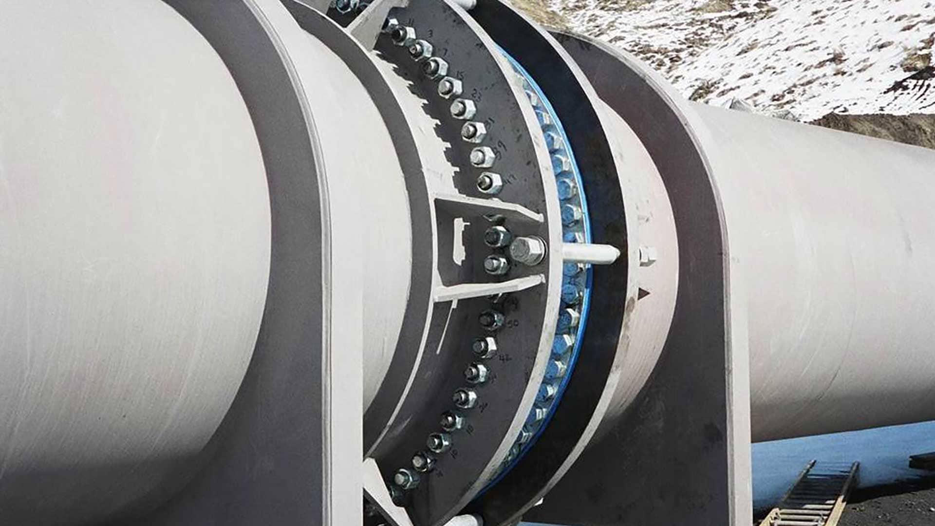 Steel water pipeline expansion joint with bolted flange connection installed above ground.