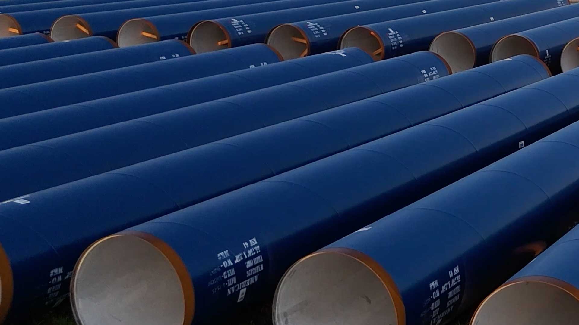 Rows of coated steel water pipes stored in a yard ready for installation.