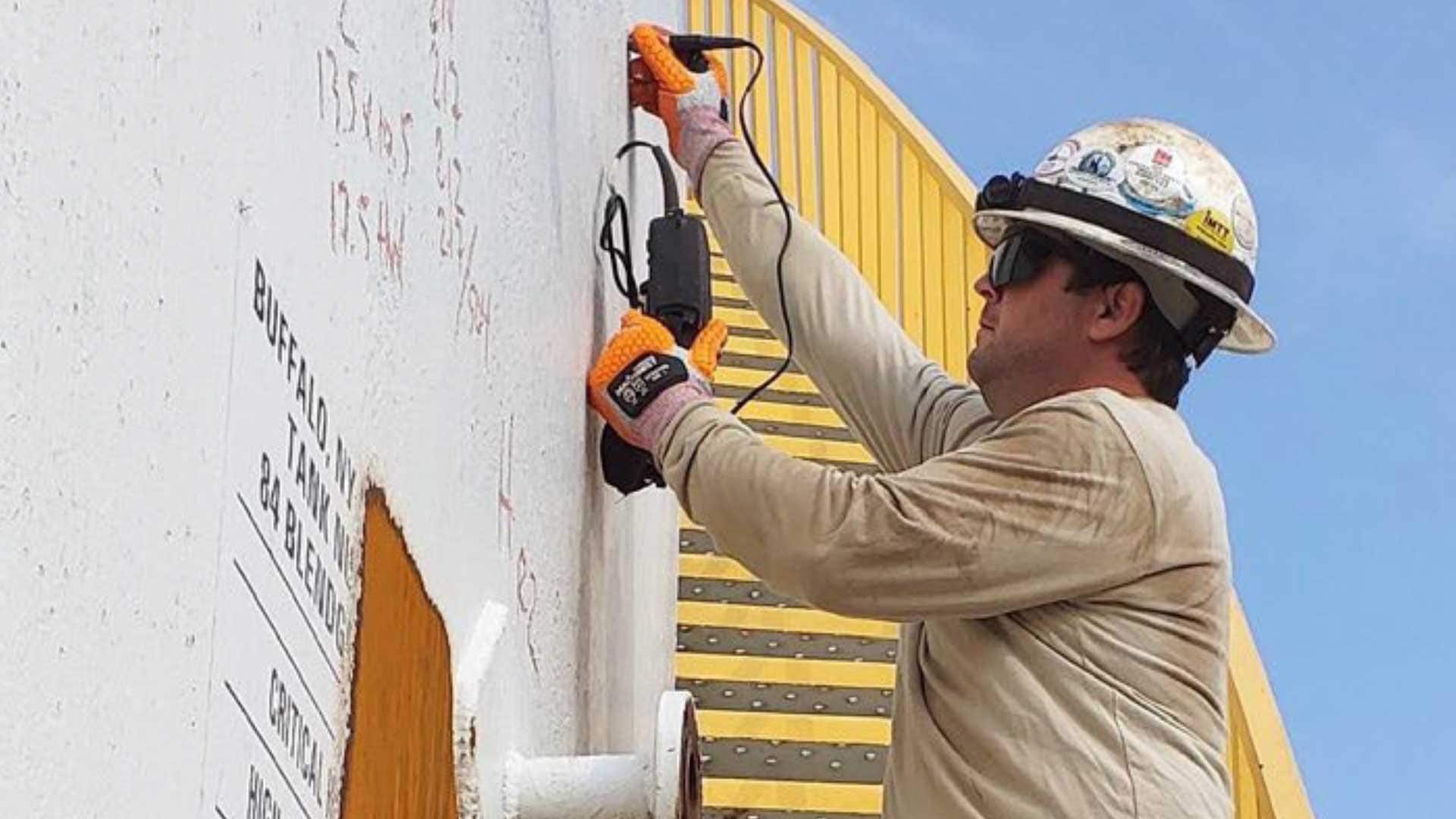 Inspector performing ultrasonic thickness testing on a steel storage tank during an API 653 tank inspection.