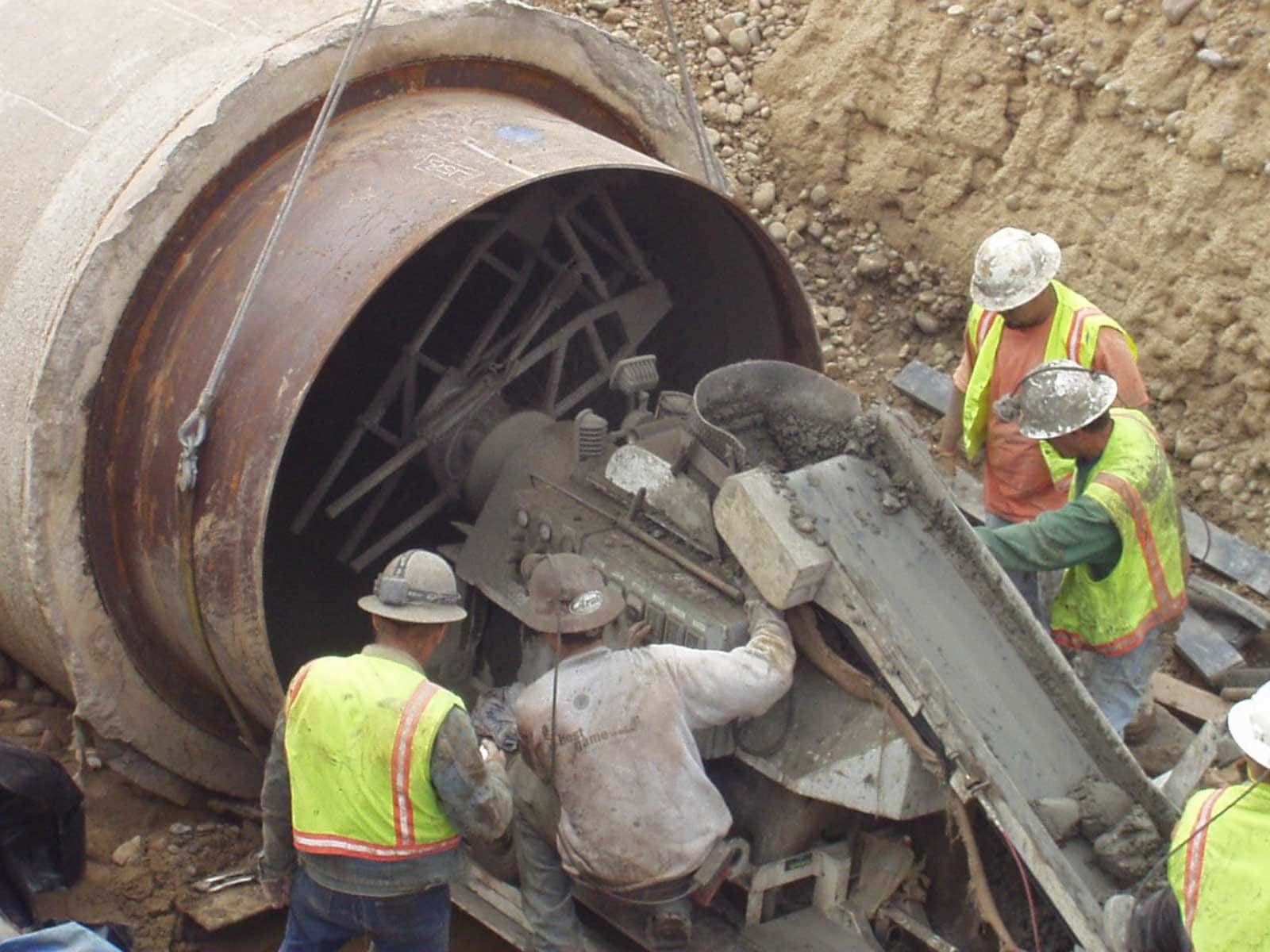Workers guide a pipe section into an existing large-diameter steel water transmission pipeline during a slip lining project.
