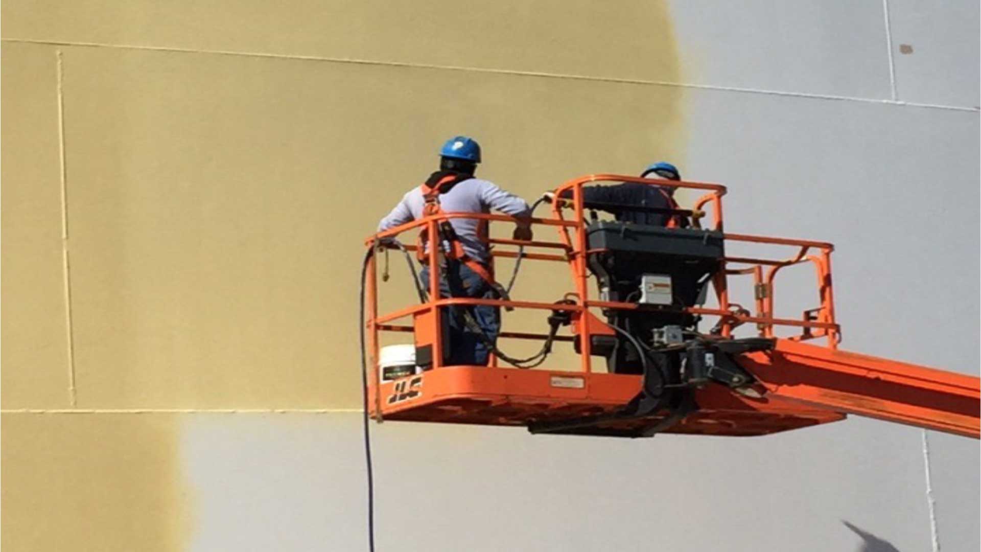 Workers applying a new protective coating to a large field-erected steel storage tank using an aerial lift.
