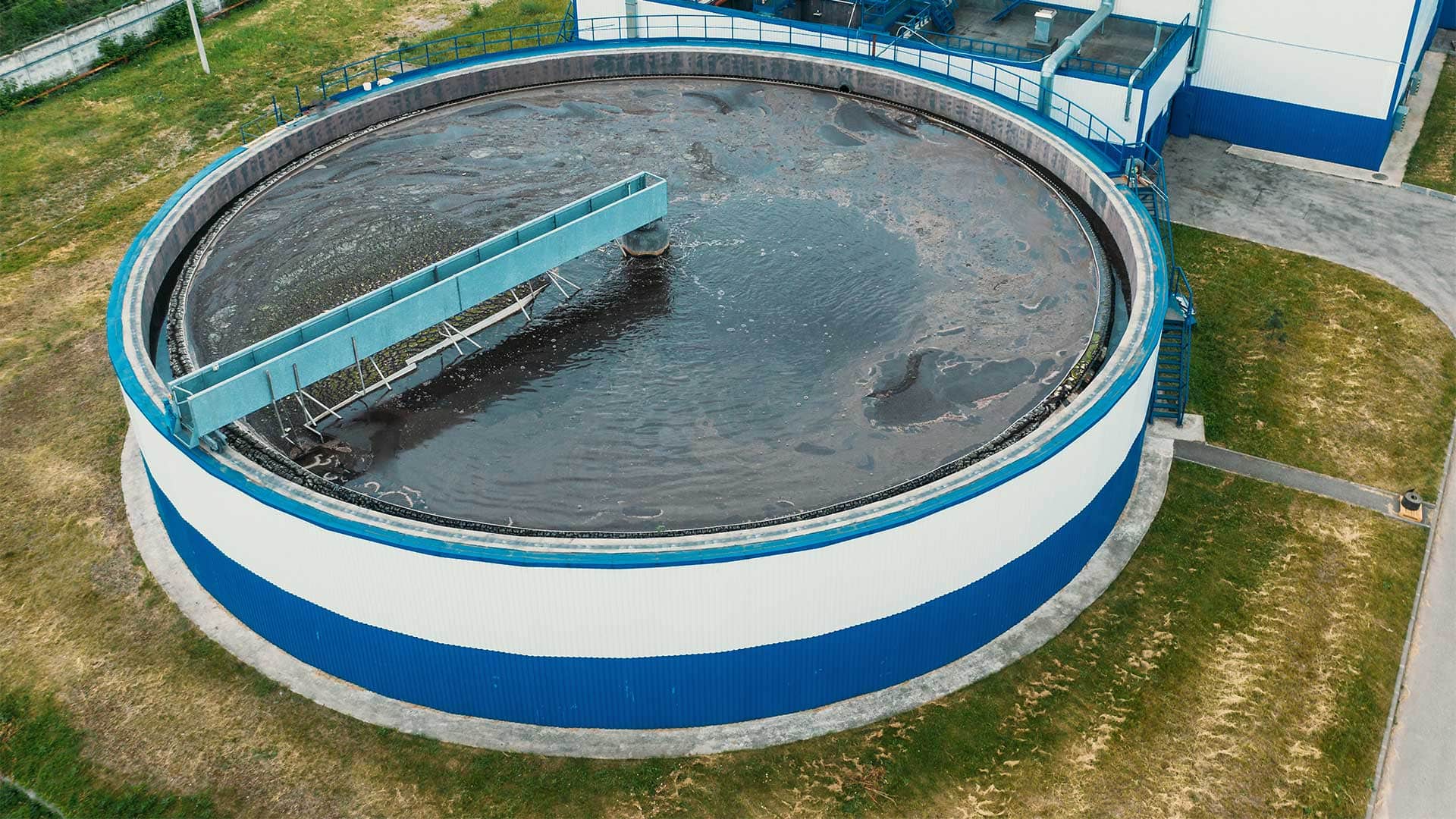 Aerial view of a circular clarifier tank at a wastewater treatment facility with a central bridge and surface solids visible.