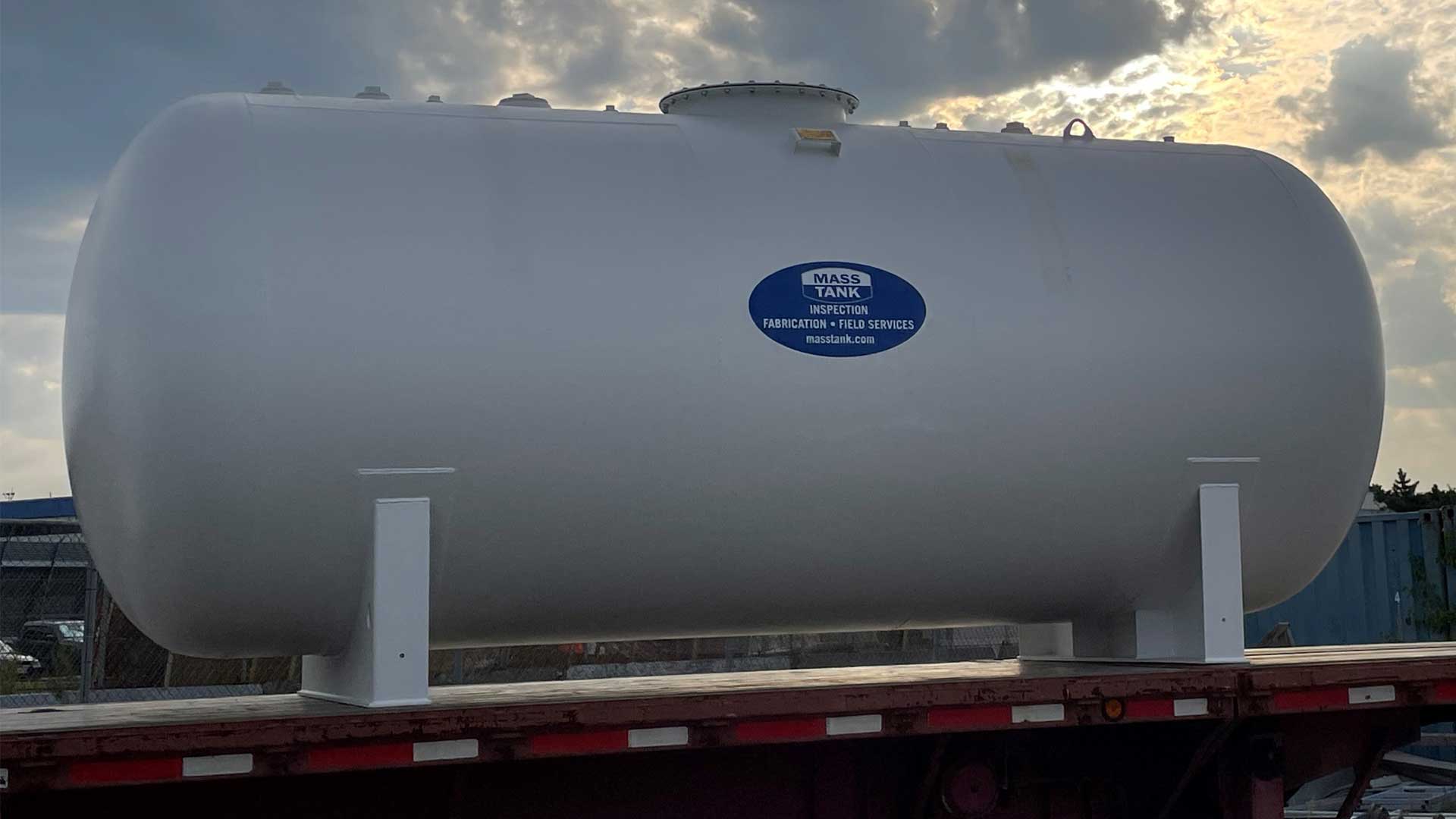 White aboveground steel fuel storage tank secured on a flatbed trailer for transport.