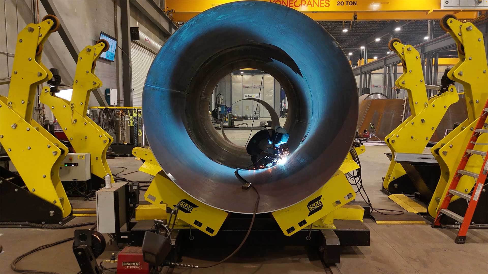 Welder fabricating a large steel tank section inside a manufacturing facility using welding positioners.