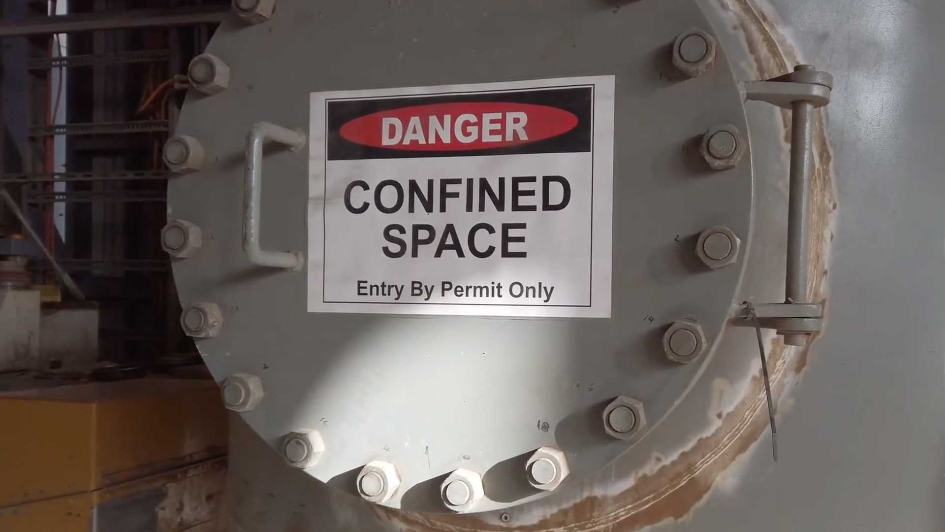 Danger confined space entry by permit only sign posted on a bolted steel tank manway.
